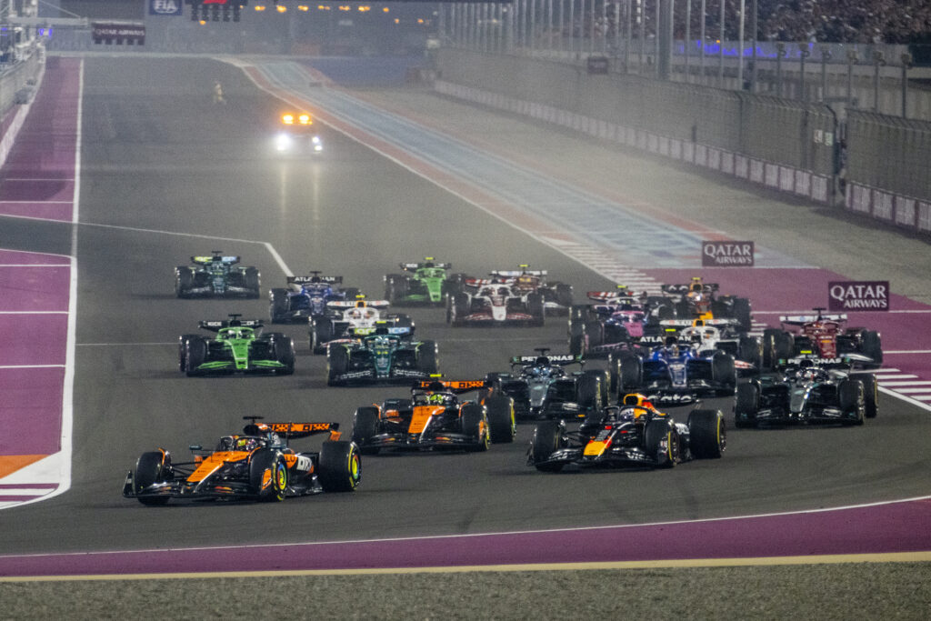 High-speed Formula 1 race cars on a night track during a Qatar Airways sponsored event.