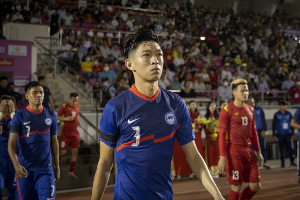 Female soccer player in blue jersey walking on field during match in Singapore.