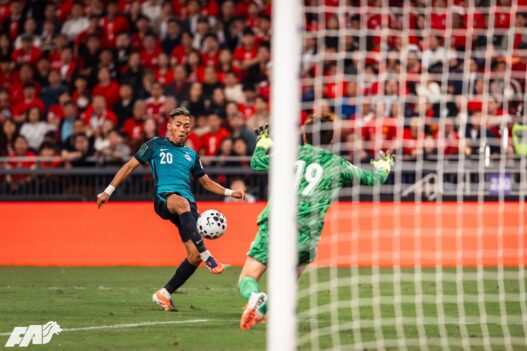Soccer player kicking ball towards goal during match in stadium.