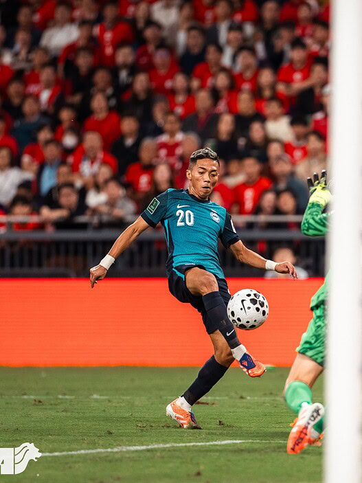 Soccer player kicking ball towards goal during match in stadium.