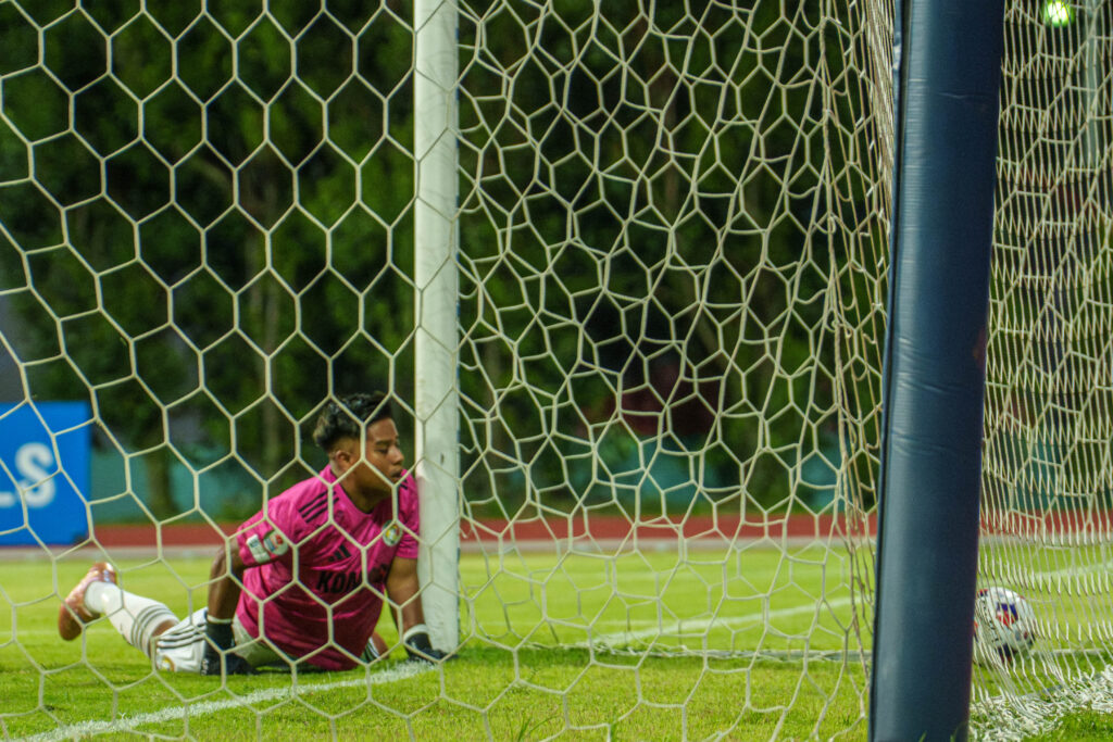 Female soccer goalkeeper diving to save a shot on goal during match.