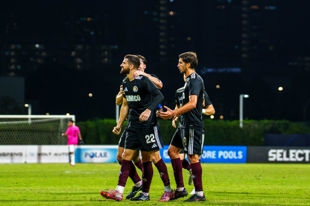 Soccer players celebrating on the field during a night match in Singapore.