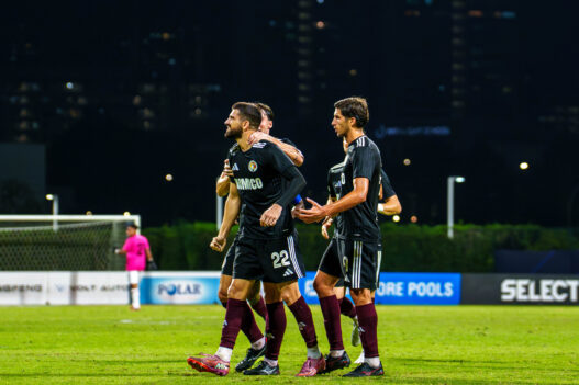Soccer players celebrating on the field during a night match in Singapore.