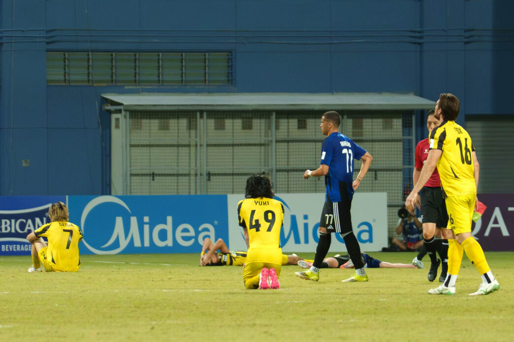 Soccer players on the field during a match, with some players sitting and others standing.