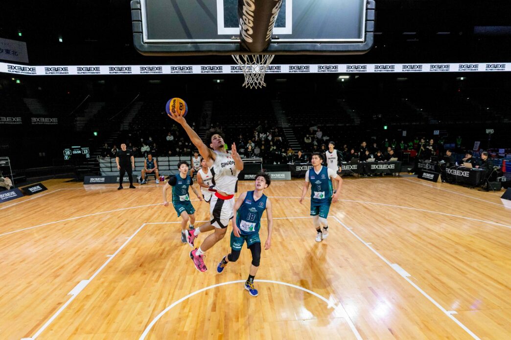 Youth basketball game in progress at an indoor court with players jumping for the ball.