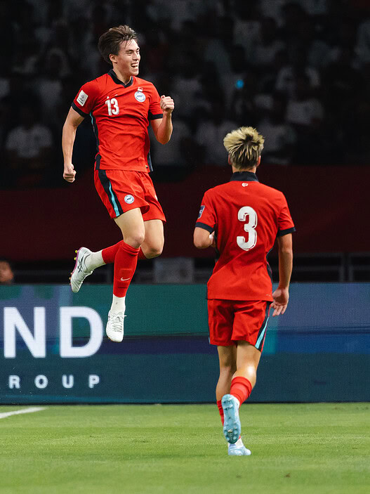 Two soccer players in red uniforms celebrating on the field during a match.