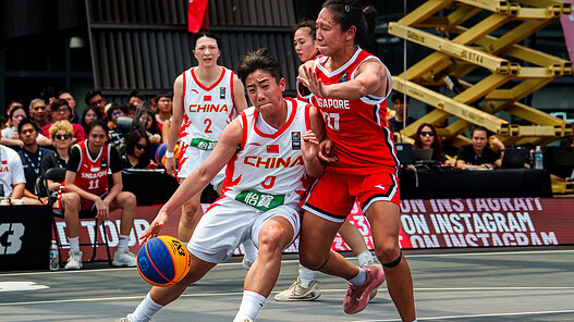 China women's basketball player struggles to control the ball against Singapore defender.