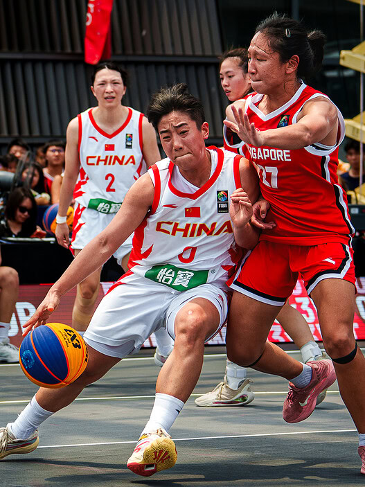 China women's basketball player struggles to control the ball against Singapore defender.